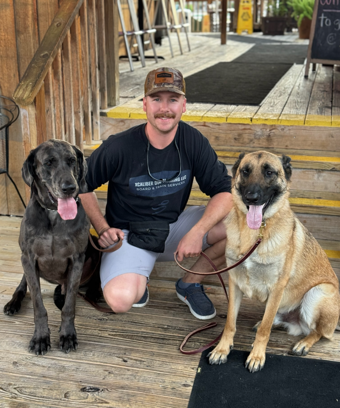 Mitchell Adcock, Marine Corps veteran and Military Working Dog Handler, kneeling with a Great Dane and a Belgian Malinois at Xcaliber Dog Training in Spring Branch, TX